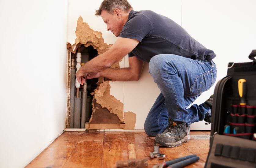 Contractor repairing burst pipe and water damaged wall during restoration